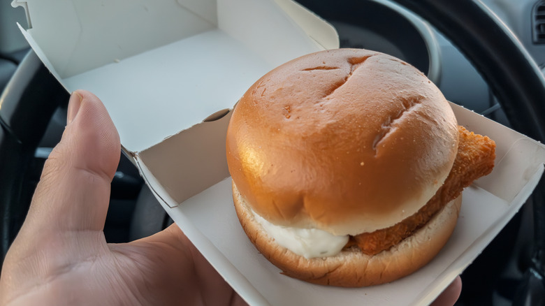 A person holding an open McDonald's box with a Filet-O-Fish inside of it in their car.