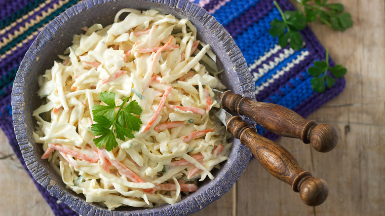 A bowl of creamy coleslaw with wooden utensils on a striped mat
