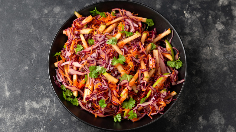 Coleslaw with shredded cabbage, apples, and carrots in a dark-colored bowl