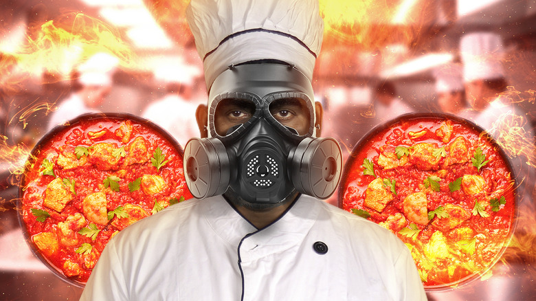 Chef wearing gas mask in front of background with flames and dishes of phaal curry