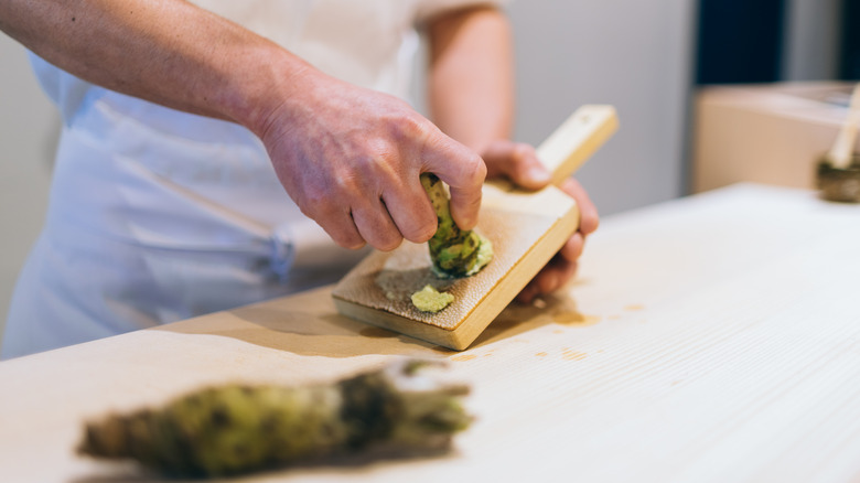 A chef grating fresh wasabi on a wooden table.