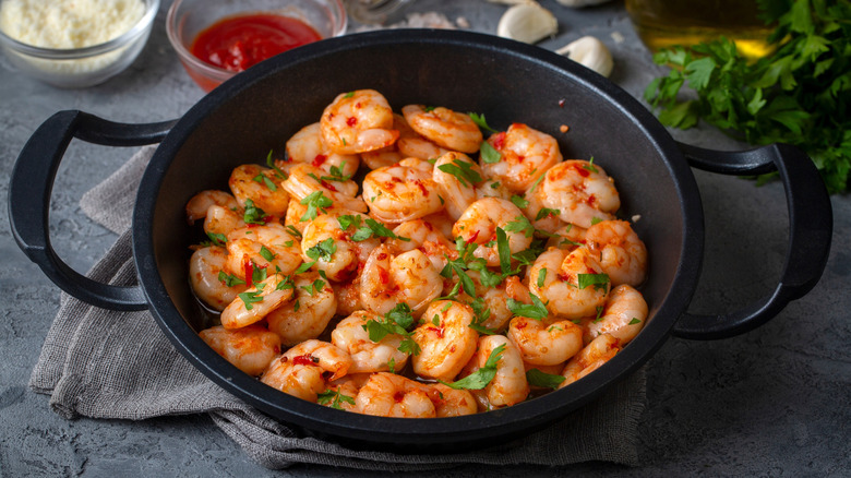 A pan filled with cooked shrimp scampi and fresh herbs
