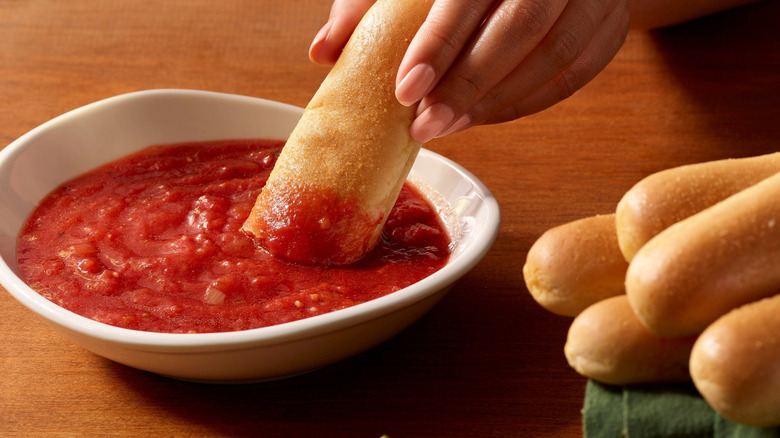 A woman dips one of her Olive Garden breadsticks into a bowl of marinara sauce on a wooden restaurant table