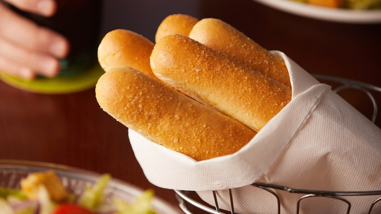Olive Garden breadsticks wrapped in a white napkin, resting in a wire basket, on a table in the restaurant