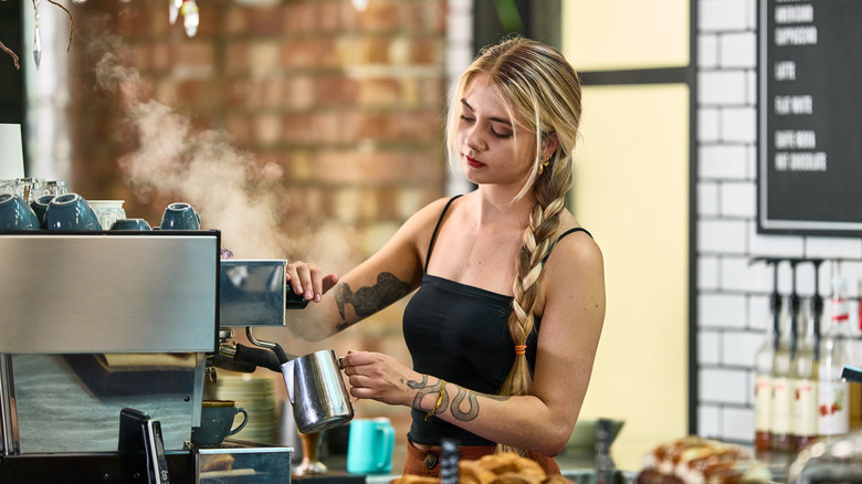 A barista calmly steams a pitcher of milk