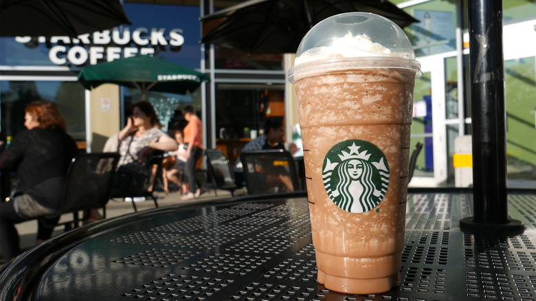 A Starbucks Frappuccino on a black table directly outside of a Starbucks location