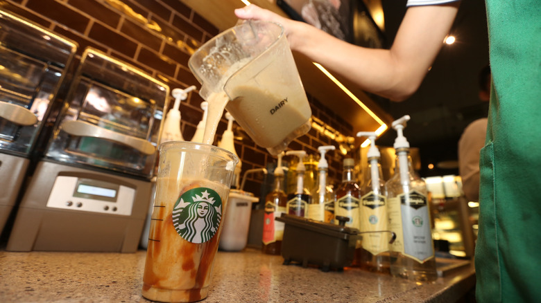 A Starbucks Barista pouring a dairy product into a plastic Starbucks cup