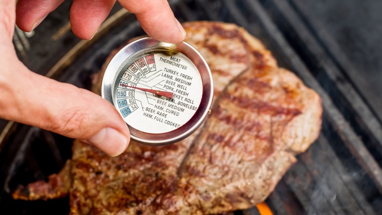Person sticking meat thermometer into steak on grill