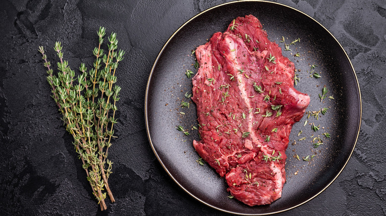 Top view of raw steak with fresh thyme on black plate
