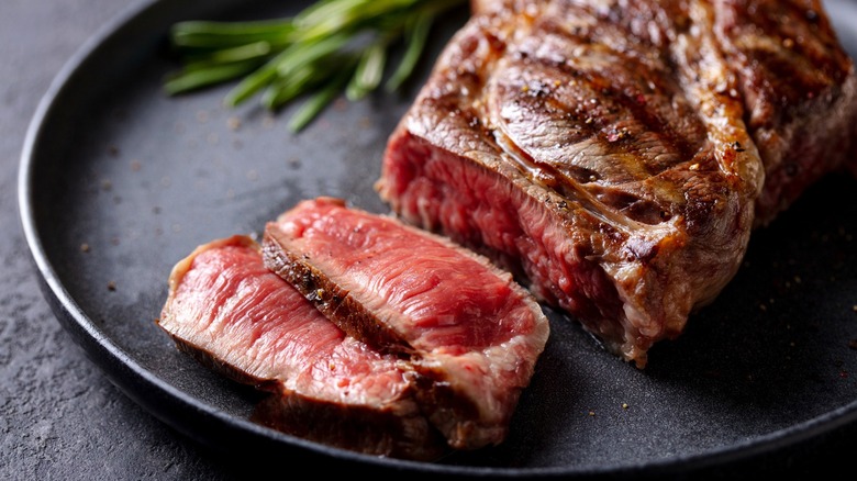 A slice of rare steak on a plate with fresh herbs