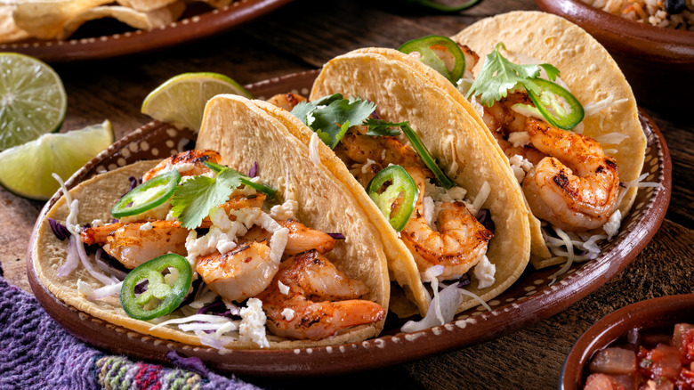 A plate of shrimp tacos with jalapeños and cilantro with Latin decor and plates.