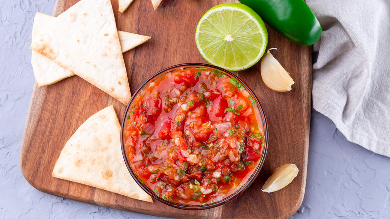 A bowl of salsa with tortillas, lime, and garlic