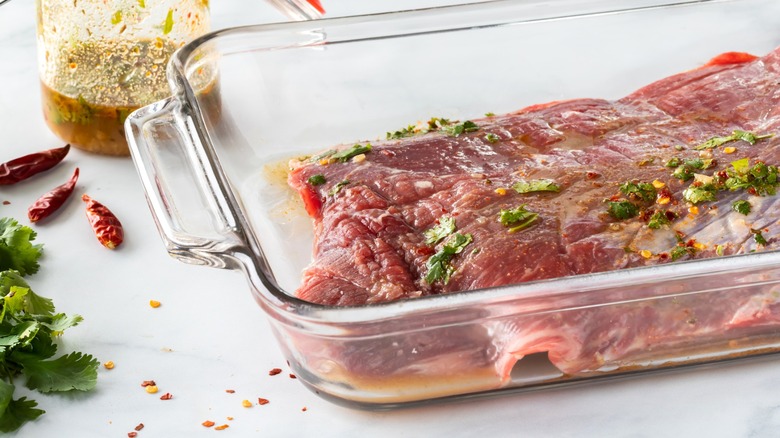 Steak marinating in lime and cilantro in glass dish