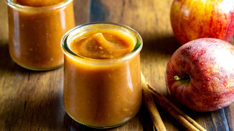 Jars of apple butter with cinnamon sticks and fresh apples on wood table