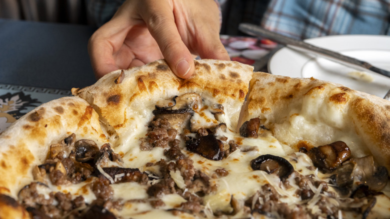 hand reaching for slice of mushroom pizza