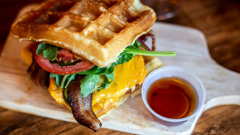 a Belgian waffle cheeseburger with maple syrup on the side on a chopping board
