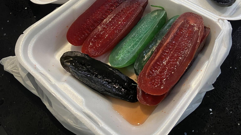 Red, green and purple Kool-Aid pickles in a styrofoam container