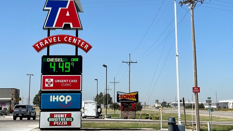 A TA Travel Center roadside sign shows diesel price at $4.49 along with signs for an urgent care clinic, IHOP, Sonic, and Hunt Brothers Pizza.