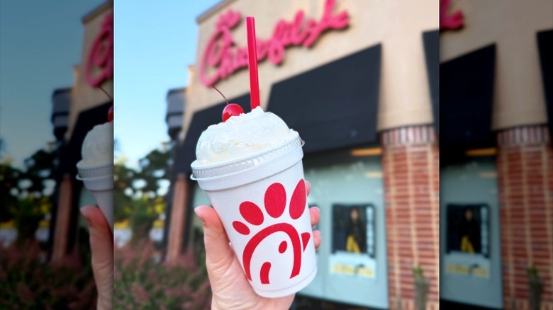 A Chick-fil-A milkshake being held up outside a Chick-fil-A location.
