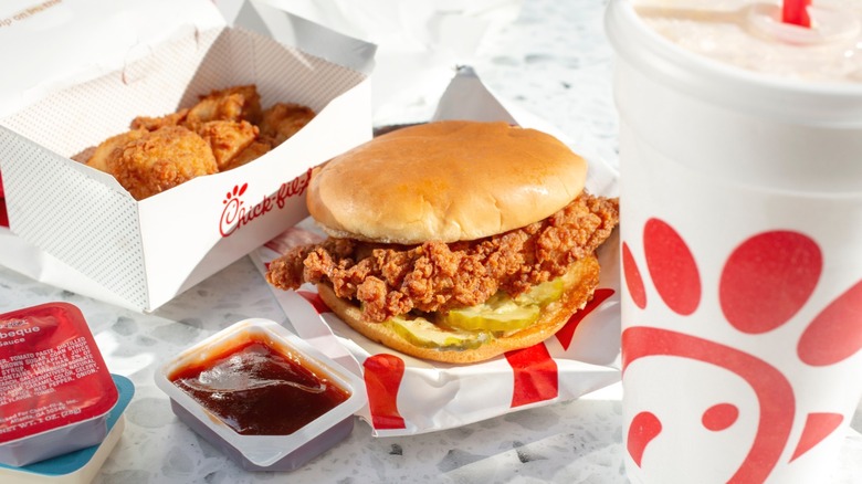 A meal from Chick-fil-A consisting of sandwich, chicken, drink, and sauces on a table