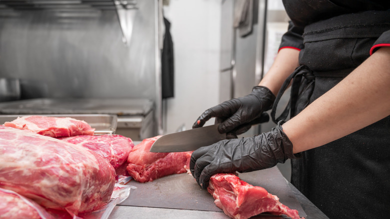Chef with gloved hands cutting raw meat