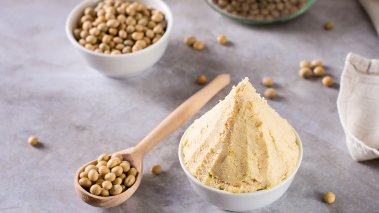 Japanese miso paste in a bowl surrounded by soy beans on a gray background