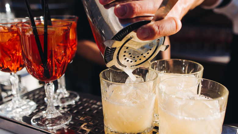 A bartender pours a citrus cocktail from a shaker