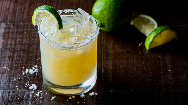 A margarita with ice, salt, and lime wedges