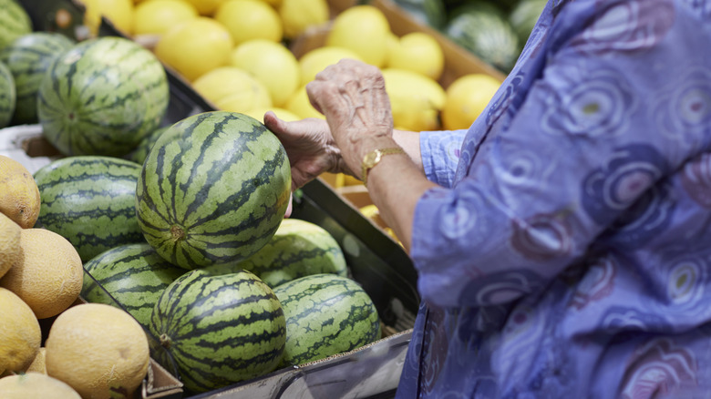 hands picking up watermelon from supermarket display