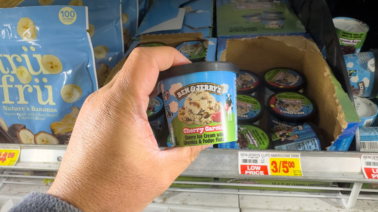 A hand holding up a small container of Cherry Garcia ice cream in a grocery aisle