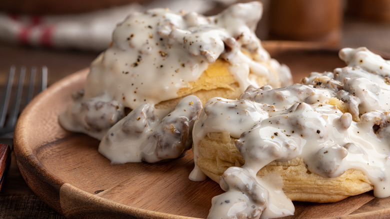Sausage gravy over biscuits on a wooden plate