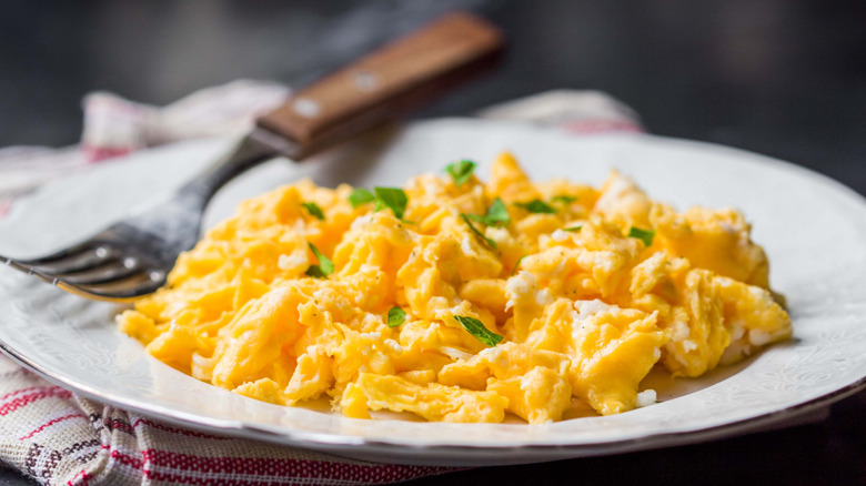 Scrambled eggs on a white plate with fresh herbs and a fork