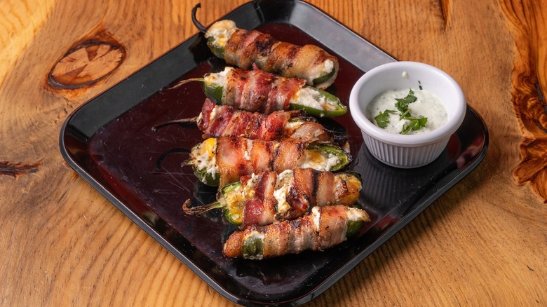 Stuffed jalapeños wrapped in bacon on black tray