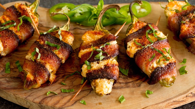 Stuffed jalapeños wrapped in bacon on wood board