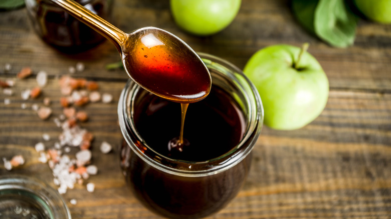 Spoon and jar of dark syrup next to green apples