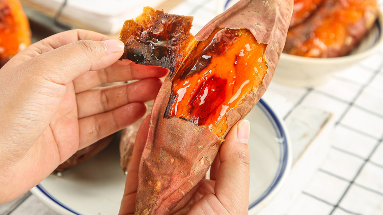 A person holds a roasted sweet potato with caramelized interior