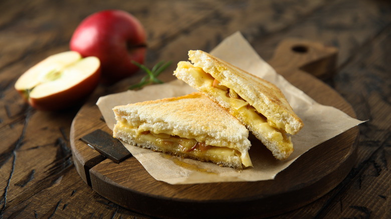 Apple grilled cheese sandwich on a wood plank with apples in the background
