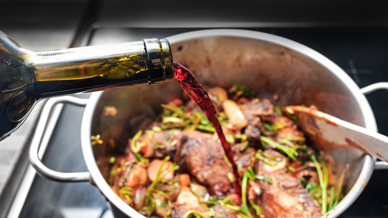 A person pouring red wine into a soup pot.