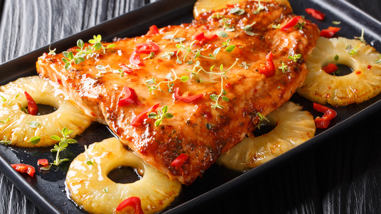 A fillet of salmon covered with glaze on top of pineapple rings in a baking tray.