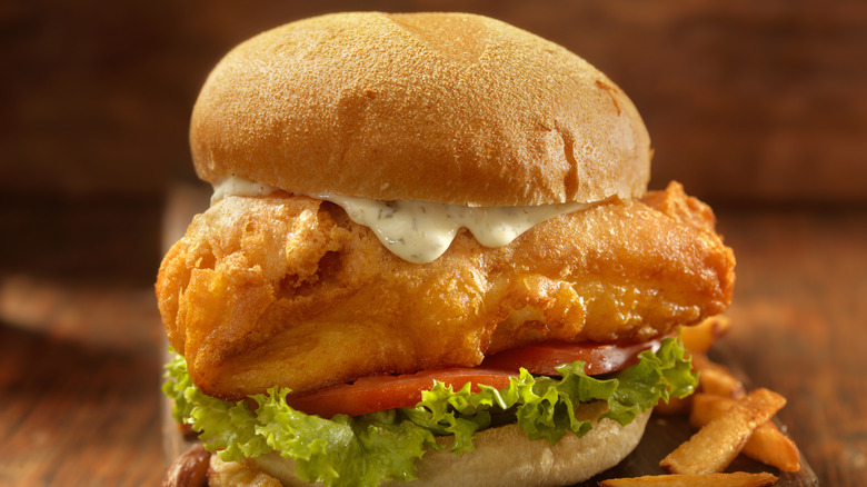 A fried fish sandwich with tartar sauce, lettuce, and tomato.