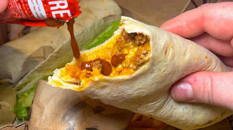 A closeup of a hand pouring fire sauce into a Taco Bell burrito
