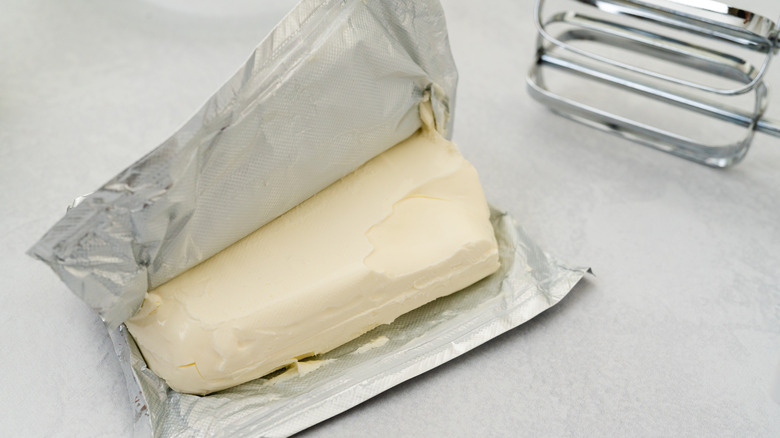 pack of softened cream cheese with hand mixer beater