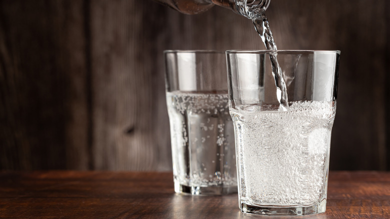 Sparkling water being poured into a glass on a dark, wooden table.