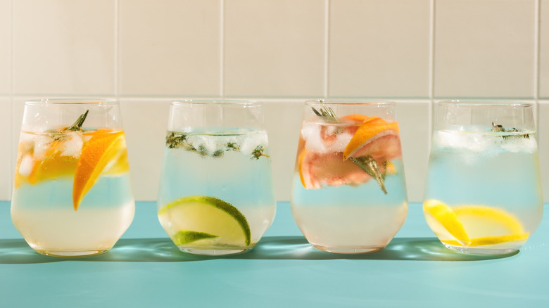 Four glasses of various citrus flavored, sparkling waters on a light table.