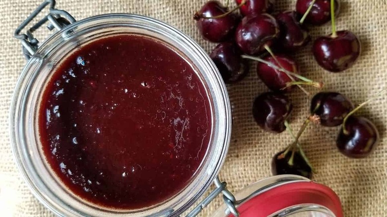 A jar of homemade barbecue sauce sitting next to cherries