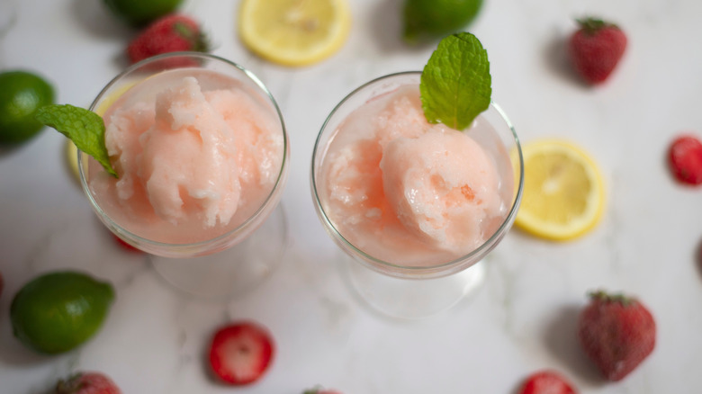 Aerial view of two small glasses of pink lemonade sorbet surrounded by fruit