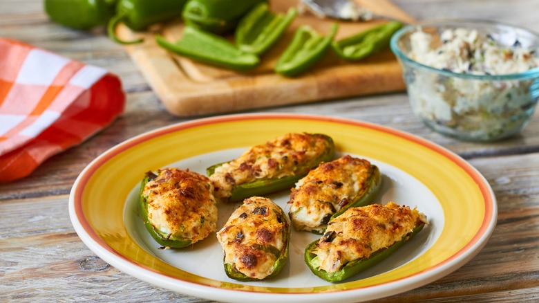 Stuffed jalapeño poppes on plate with sliced jalapeños in the background.
