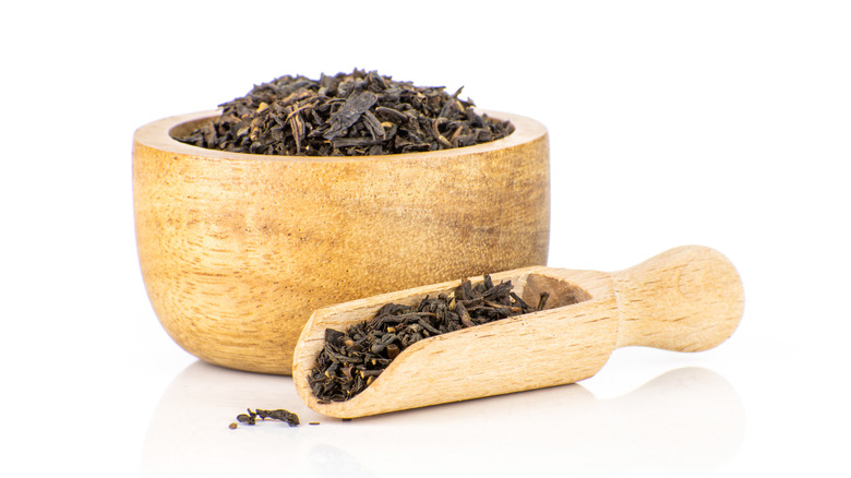 An abundance of loose leaf Earl Grey tea pieces inside a wooden bowl and wooden spoon