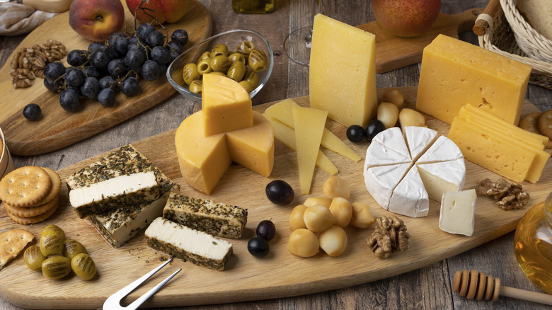 A charcuterie board displaying several types of hard and soft cheeses with nuts, fruits, olives, and crackers