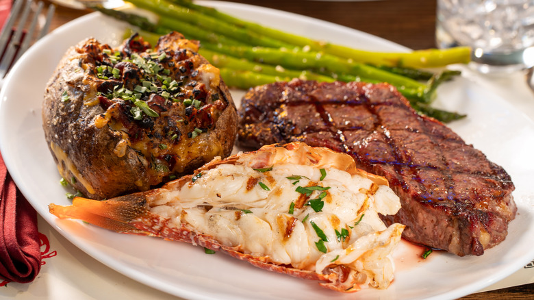 Dinner plate with whole steak, lobster tail, loaded baked potato, and asparagus